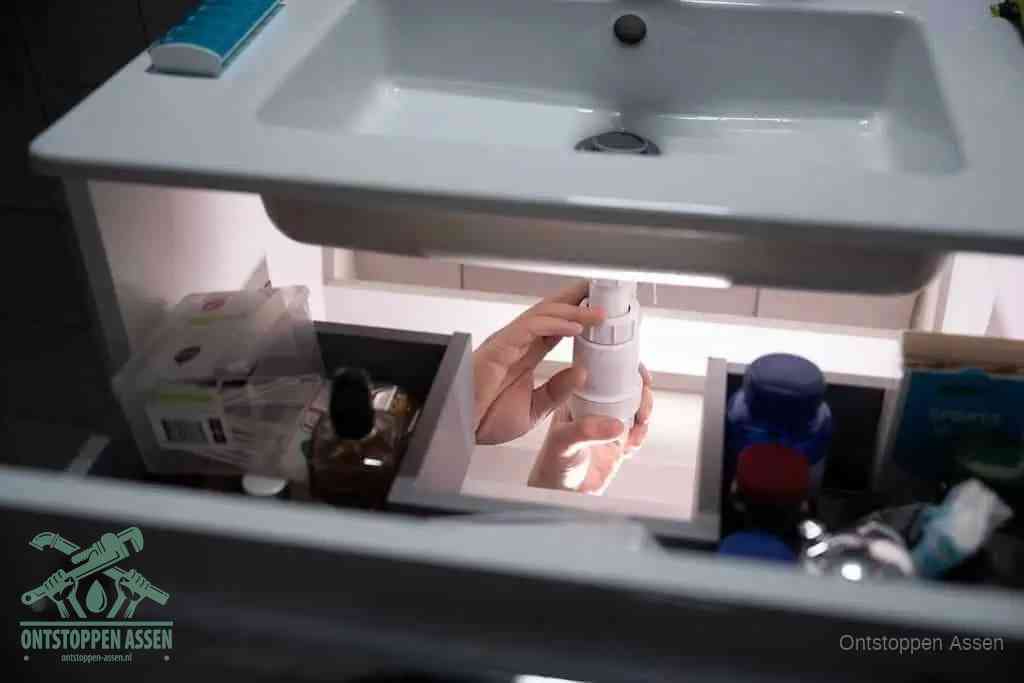Een pompfles met zeep boven een wastafel, de heet water en afwasmiddel-methode om een vetprop in de afvoer los te maken in Assen