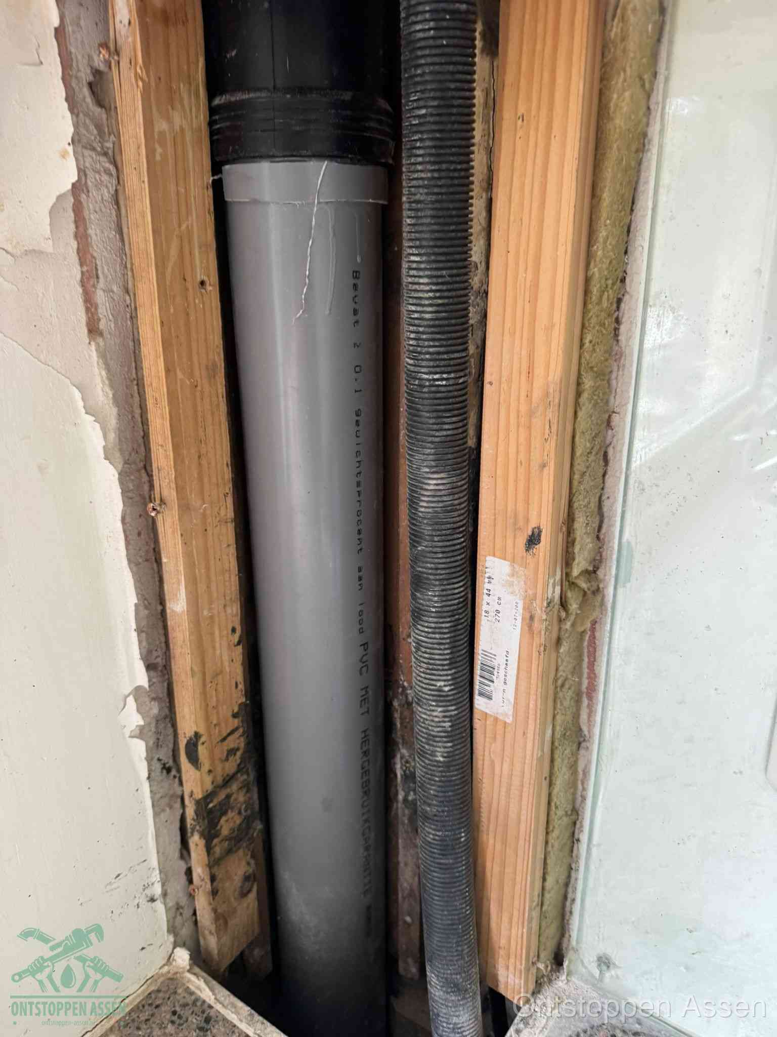 Een grijze PVC-afvoerbuis met een flexibele ribbelslang in een open wandconstructie, een verwaarloosde afvoer die te lang is blijven zitten in Assen