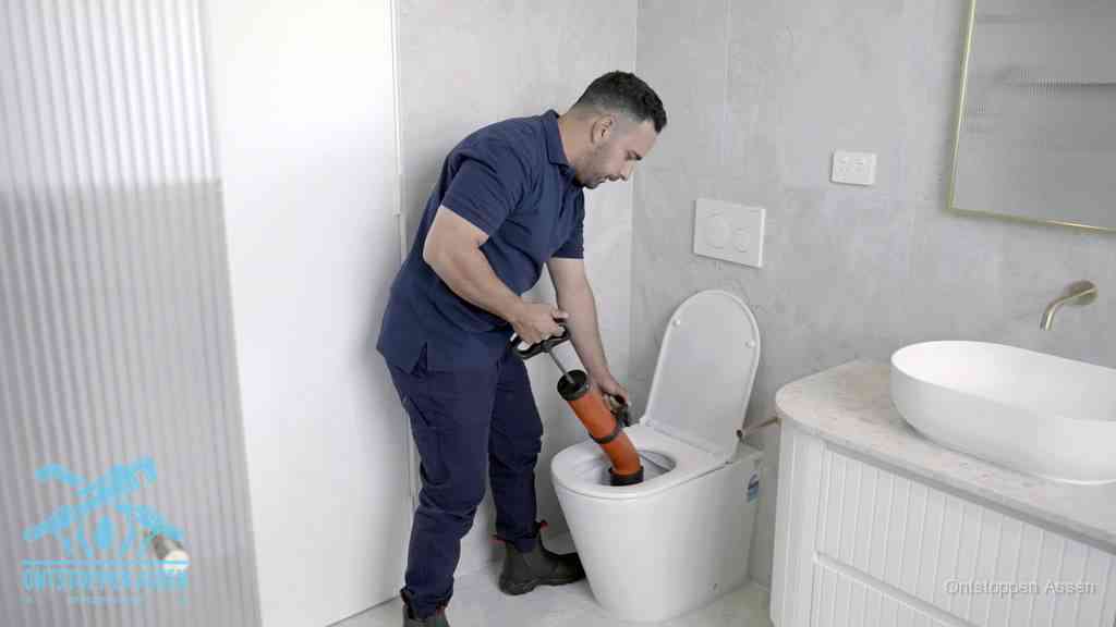 Een monteur buigt over een wandcloset en duwt met de hand een persluchtontstopper in de toiletpot om de verstopping handmatig los te maken in Assen