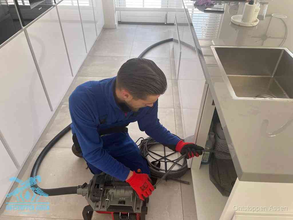 Een monteur ontstopt de keukenafvoer onder de spoelbak met een elektrische veermachine in Assen