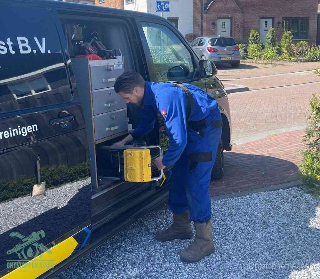 Een monteur pakt buiten op de oprit gereedschap uit de bedrijfsbus, het moment om een professional in te schakelen voor een verstopte afvoer in Assen