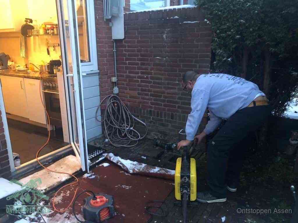 Een monteur werkt buiten bij een open riool-/grondput met een elektrische ontstoppingsmachine om een verborgen afvoerprobleem op te sporen in Assen