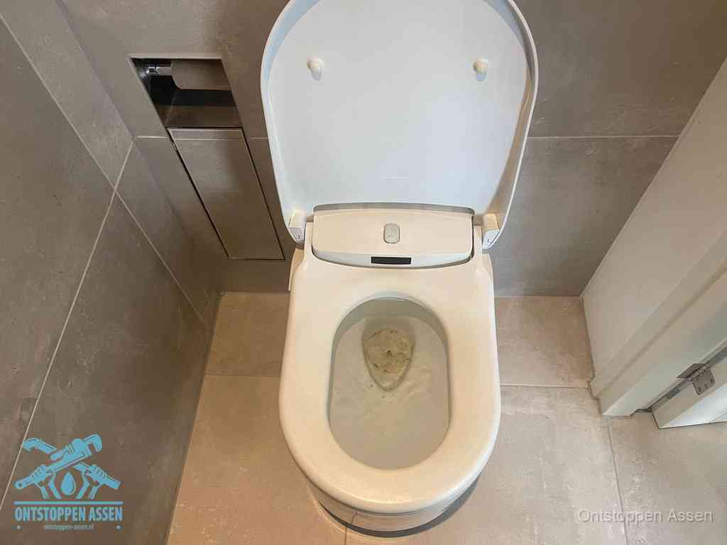 Een wit hangtoilet waarin een prop wc-papier op het water blijft drijven, een duidelijk signaal van een verstopte wc in Assen