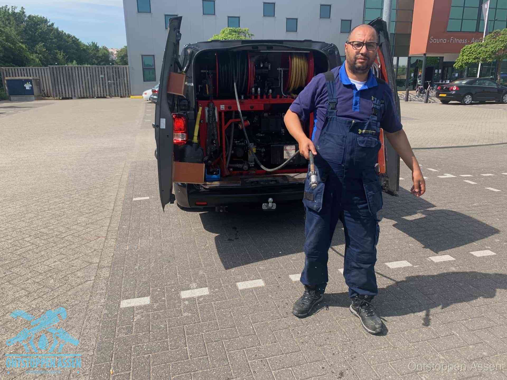 Een monteur bij zijn bestelbus met een hogedruk- en rioolreinigingsunit, klaar om de oorzaak van terugkerende wc-verstoppingen aan te pakken in Assen