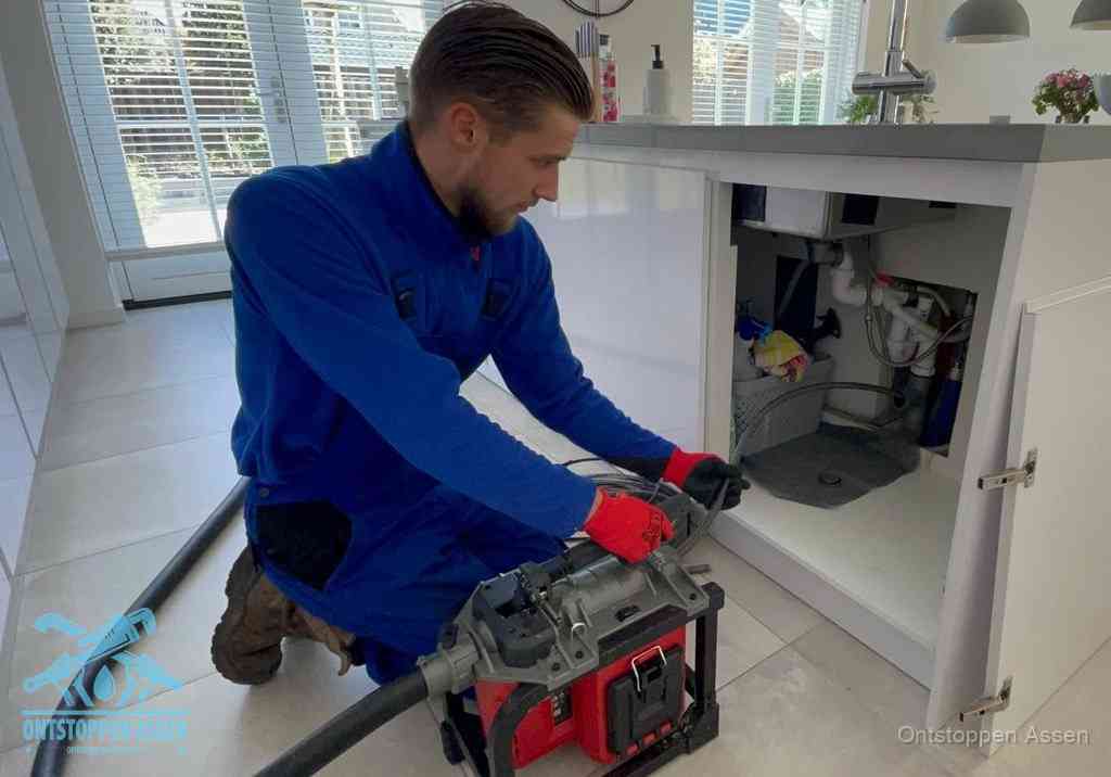 Een monteur voert een professionele elektrische ontstoppingsmachine in de afvoer onder de spoelbak tijdens het gootsteen ontstoppen in Assen